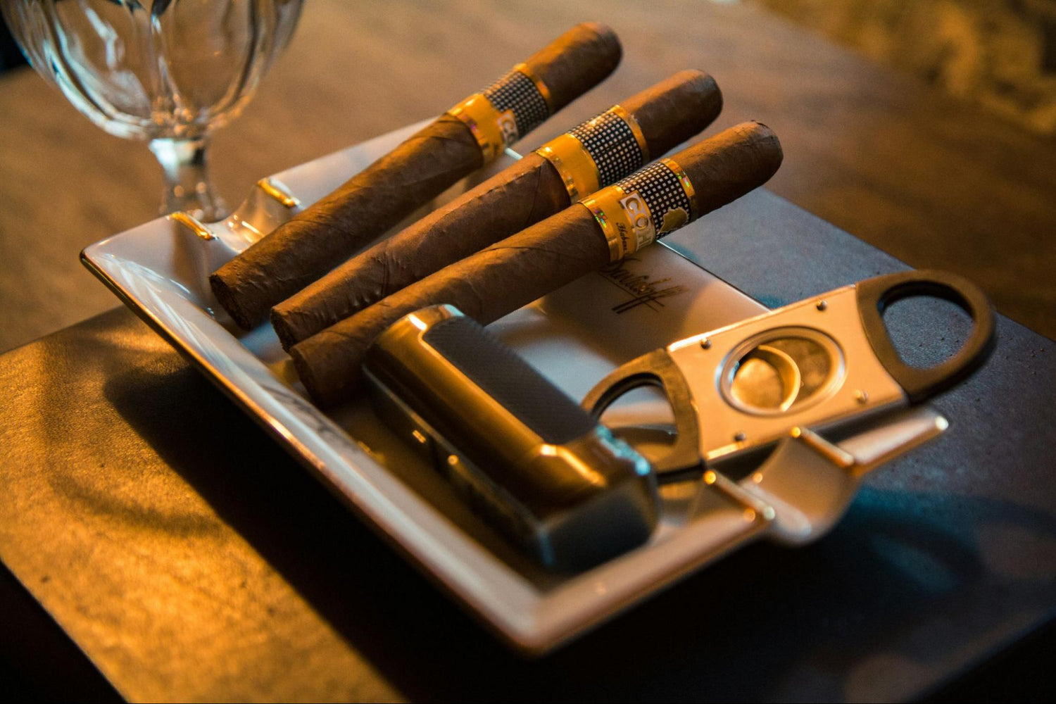 Three cigars and a cigar cutter on a table.