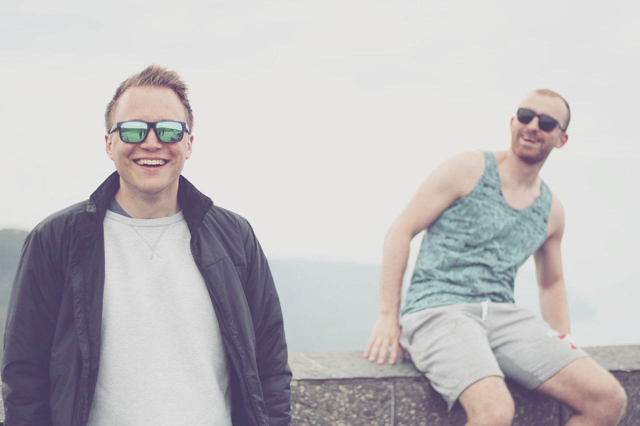 Two smiling men are on a stone bridge over water.