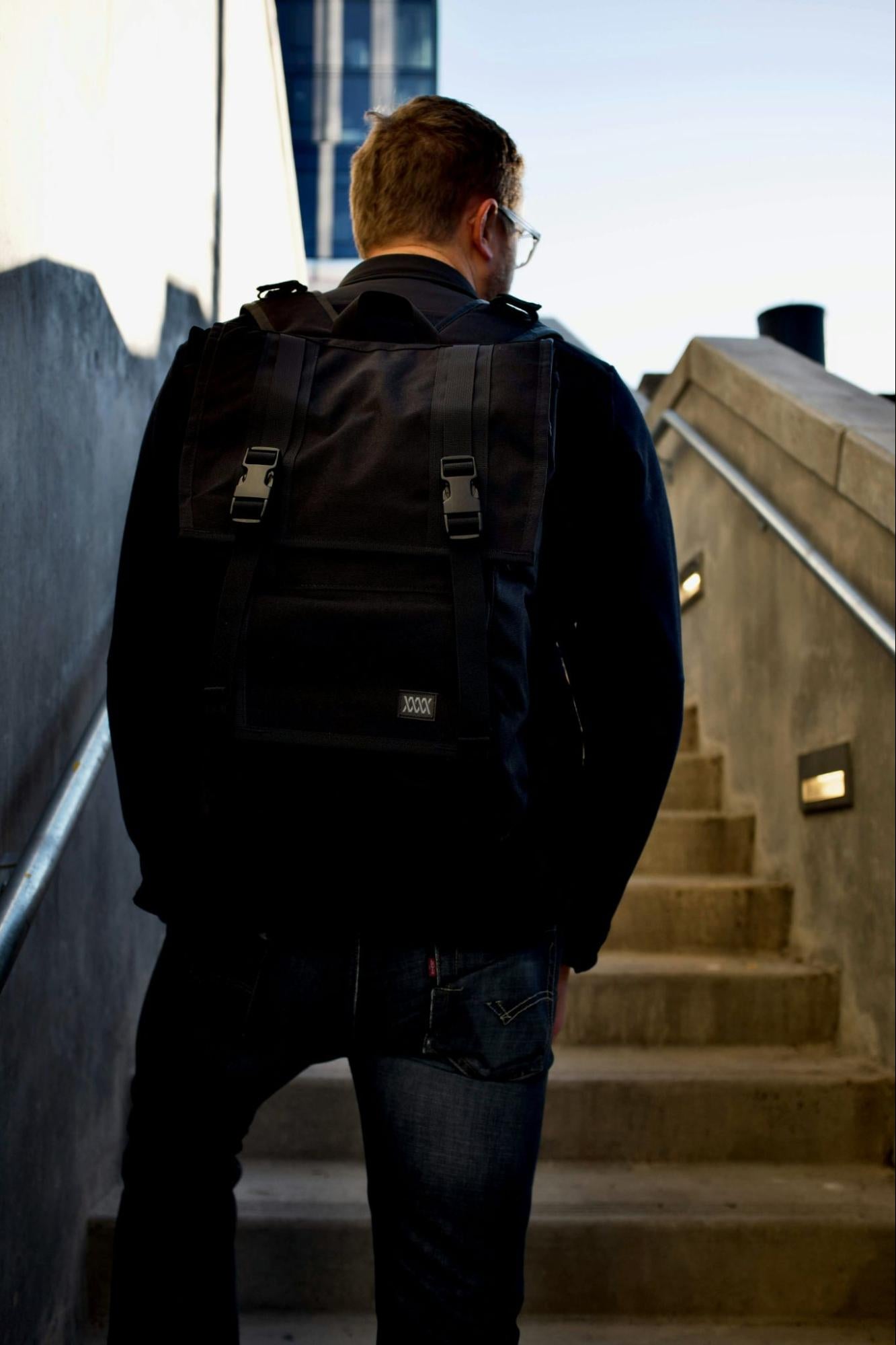 A man wearing a backpack with everyday carry items walks up steps.